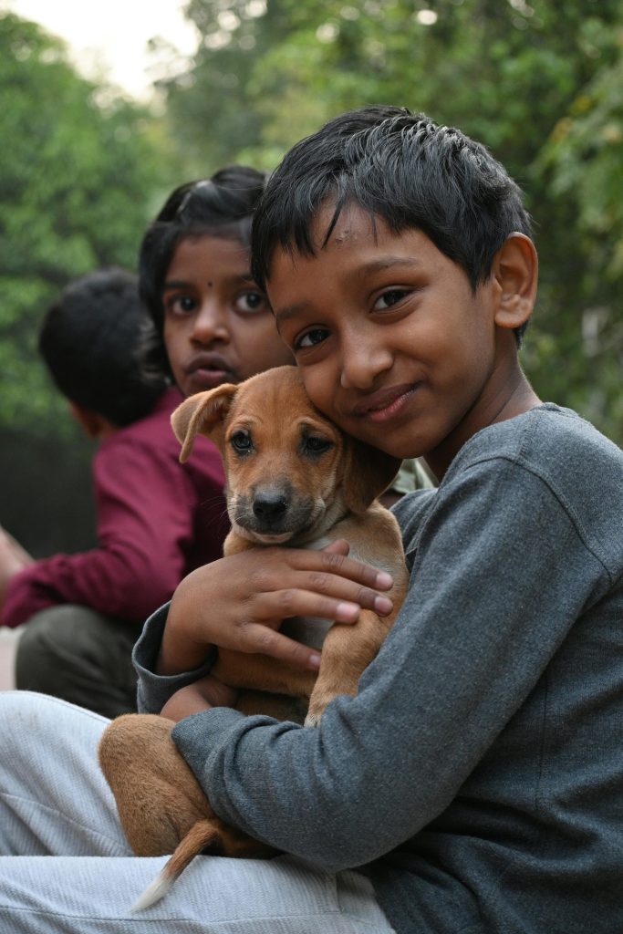 niños indios sostienen en sus brazos a un cachorro canino, son 3 niños sentados en fila