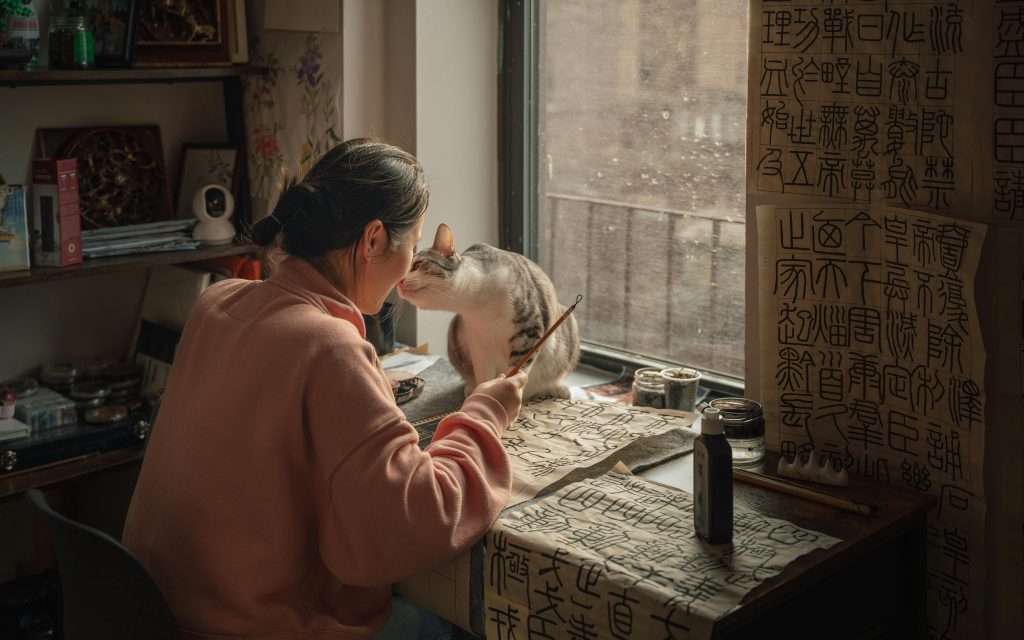 mujer sentada trabajando en su escritorio con su gatita sobre la mesa y donde se hacen cariño mutuo