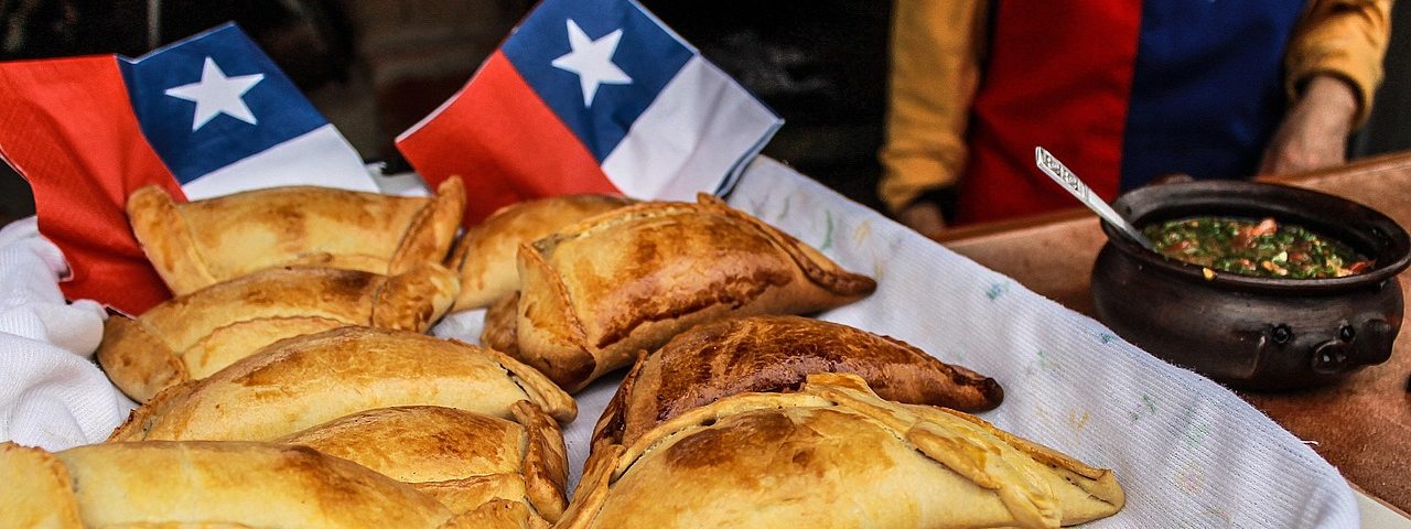 mesa con empanadas sobre un mantel blanco y servilletas al fondo con el diseño de la bandera chilena