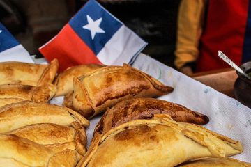 mesa con empanadas sobre un mantel blanco y servilletas al fondo con el diseño de la bandera chilena