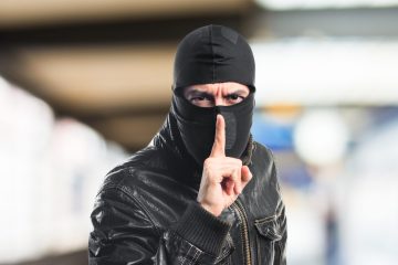 hombre con pasamontaña negra y chaqueta de cuero negra señalando silencio es un ladrón