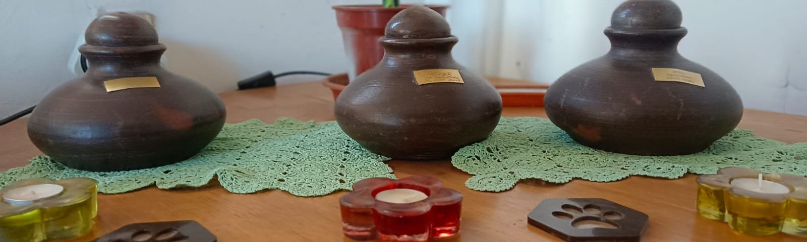 tres anforas de perritos puestas en linea sobre una mesa de madera cada una con una velita y un posa vasos de huellita animal