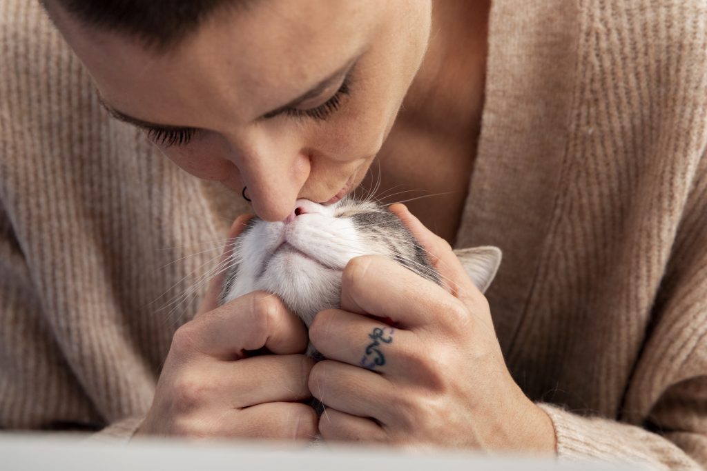  donde se ve que ella tiene a su gatito sostenido de su cabecita por detras y le esta dando un besito con mucho amor sobre el tabique de la nariz de gatito