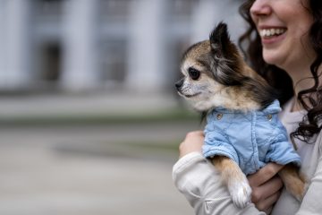 vista lateral de una mujer con un perro chihuahua en su brazos que esta utilizando una parka celeste