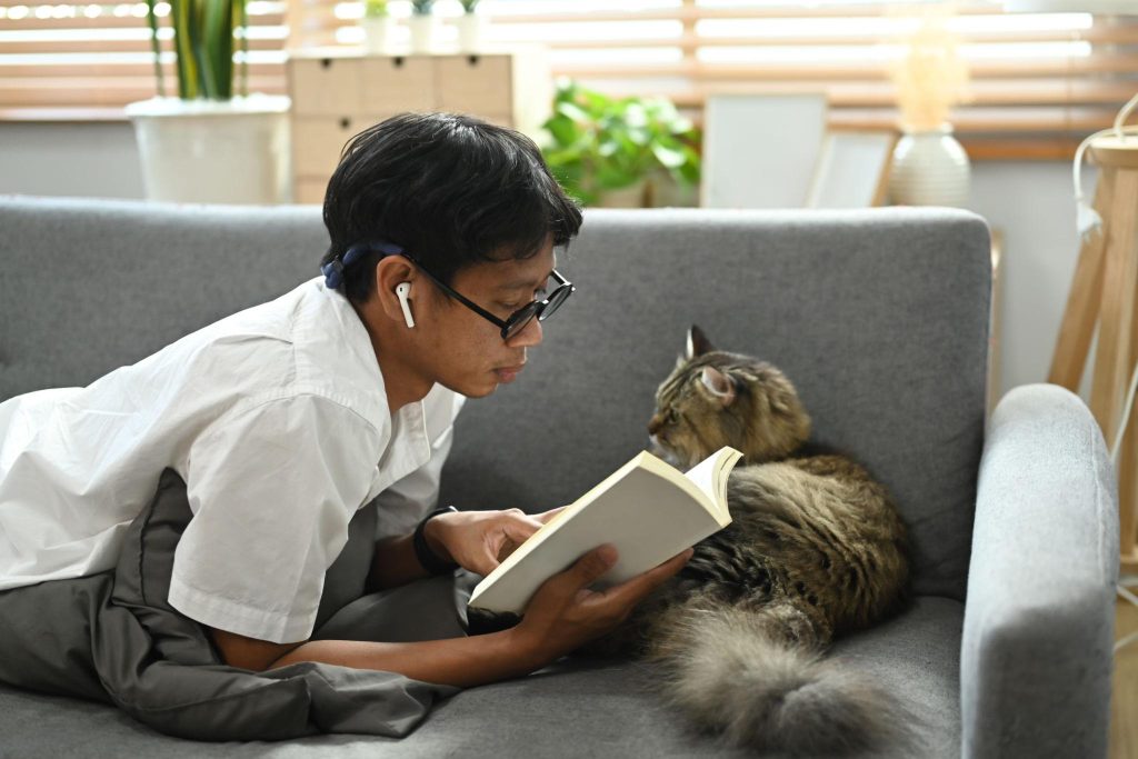 tutor tendido leyendo junto a su gato en el sofá