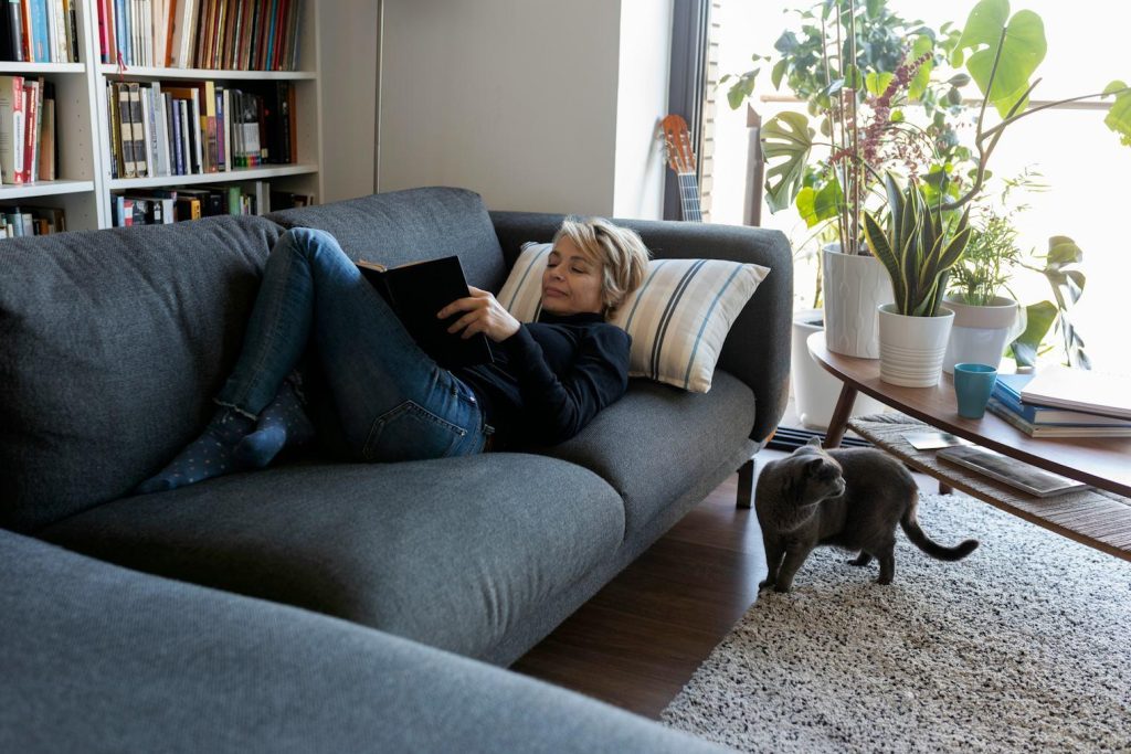 tutora tendida leyendo un libro en el sofá y su gato de ambula en el piso